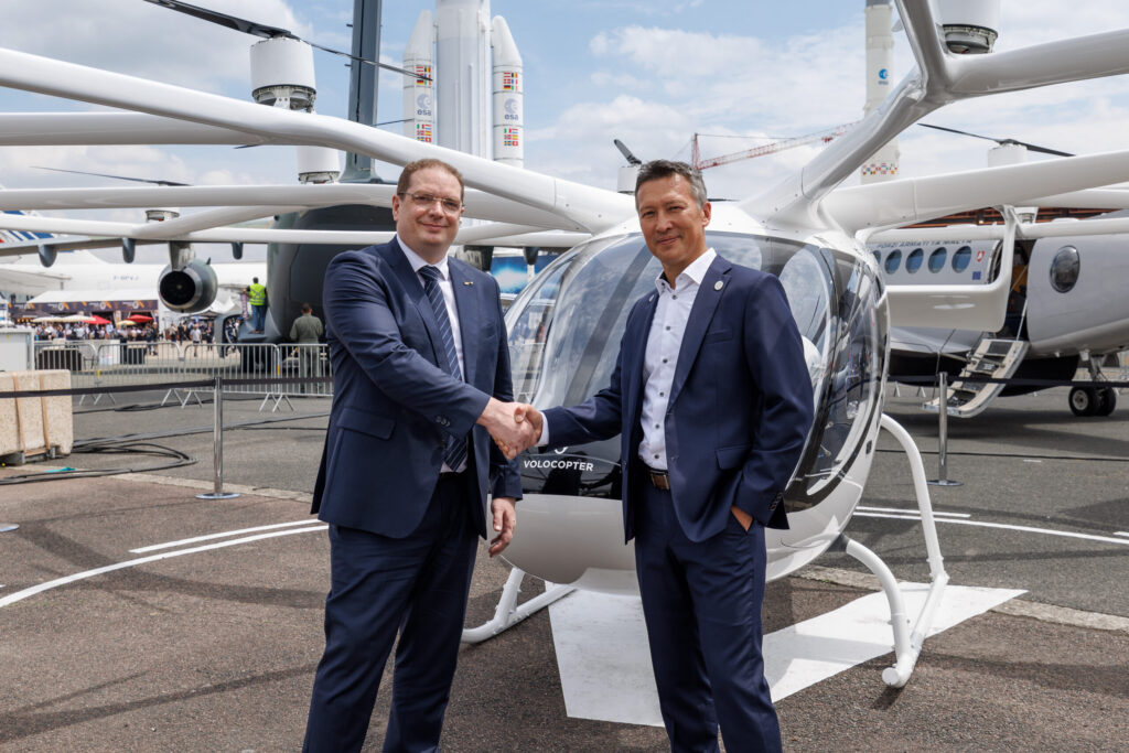 An image showing Frédéric Bruder — Chief Executive Officer of ADAC Luftrettung & Dirk Hoke — CEO of Volocopter shaking hands in front of an eVTOL vehicle