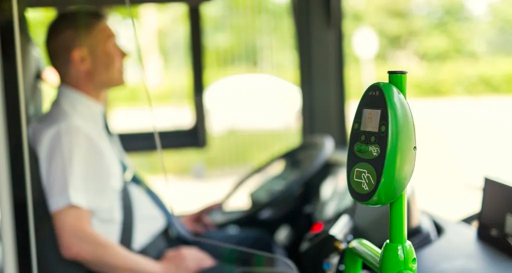 A bus driver sat next to a green contactless bus payment device