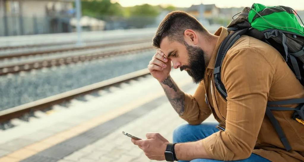 A man sitting by the train tracks, looking worriedly at his phone