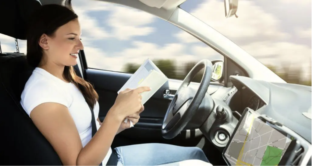 An image of a woman reading whilst in the drivers seat of a moving car