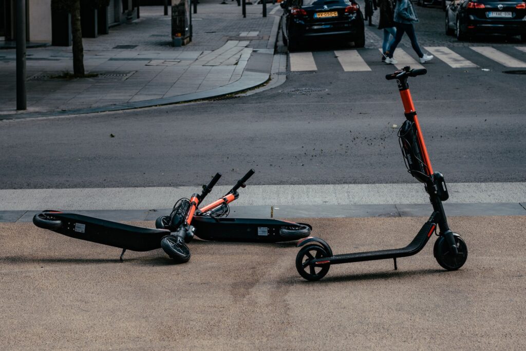 Red electric scooters parked in the middle of the pavement. Two scooters are on their sides