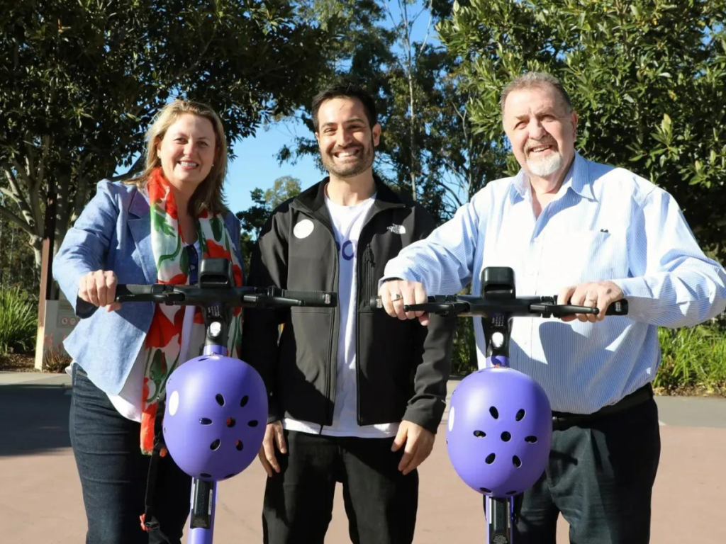 Three people smiling whilst holding Beam e-scooters