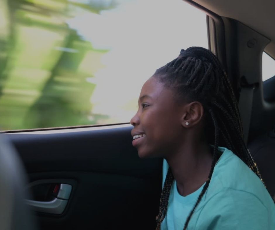 A girl smiling whilst looking out of a car window