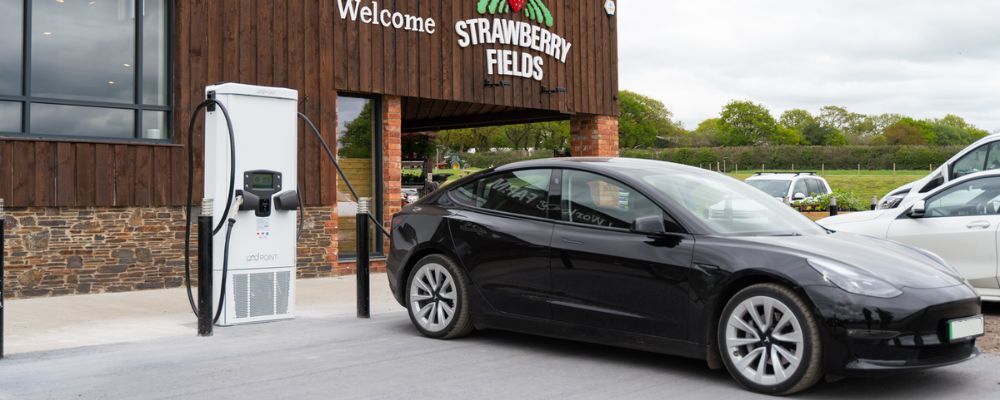A black car charging outside Strawberry Fields grocery store