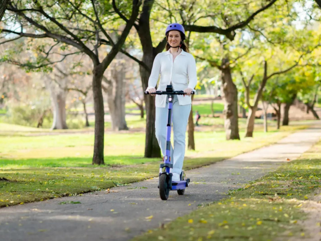 An image showing a woman riding through a park on an eScooter
