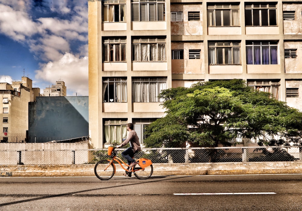 A man rides past an apartment building on an orange e-bike