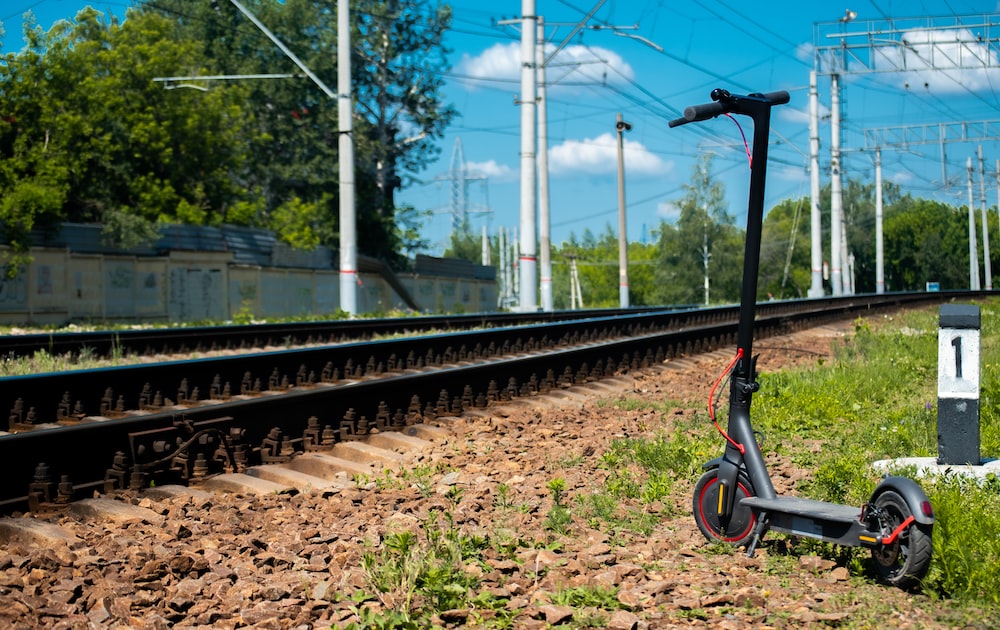 An electric scooter parked next to a train track on a sunny day