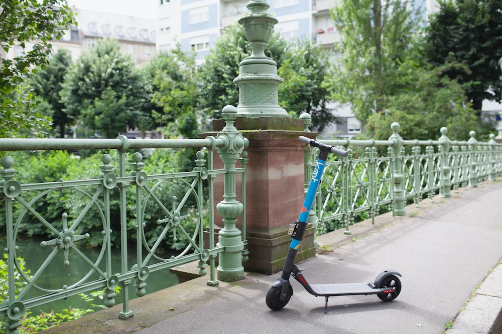 A blue e-scooter parked on an ornate sage green bridge