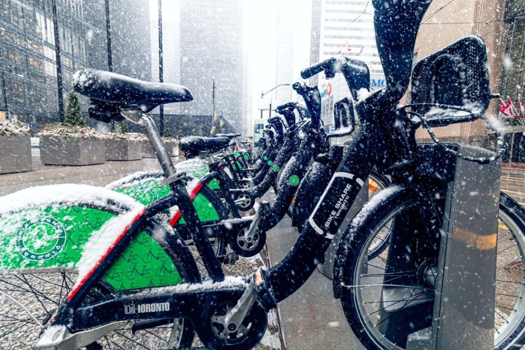 Several parked "Bike Share Toronto" e-bikes with snow falling on them