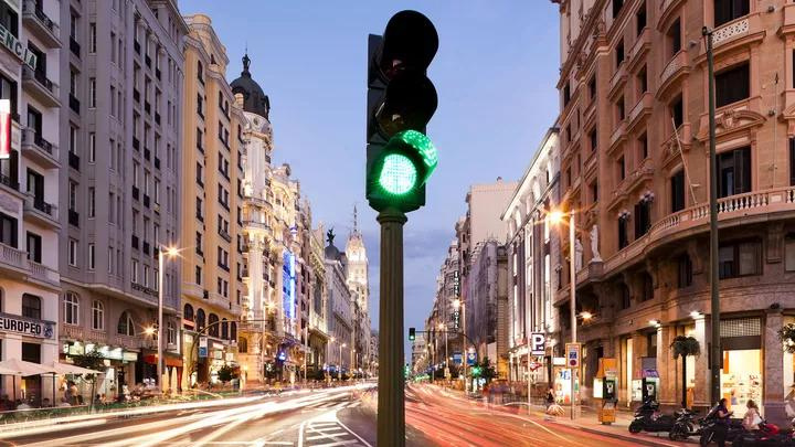 Gran Via road in Madrid at night. In the centre of the image is a traffic light on green