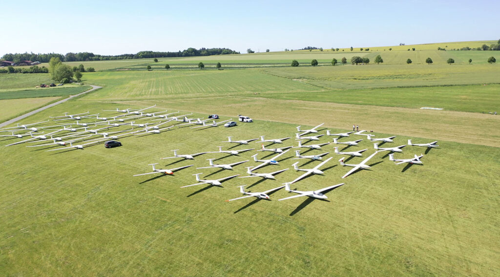 30+ white gliders parked in neat squares on a grassy field