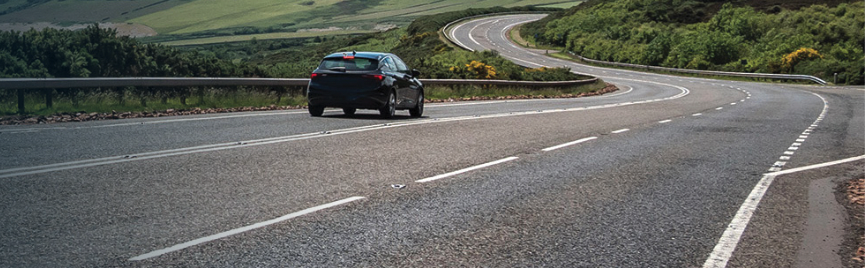 A car driving along an empty road, in the background are green hills