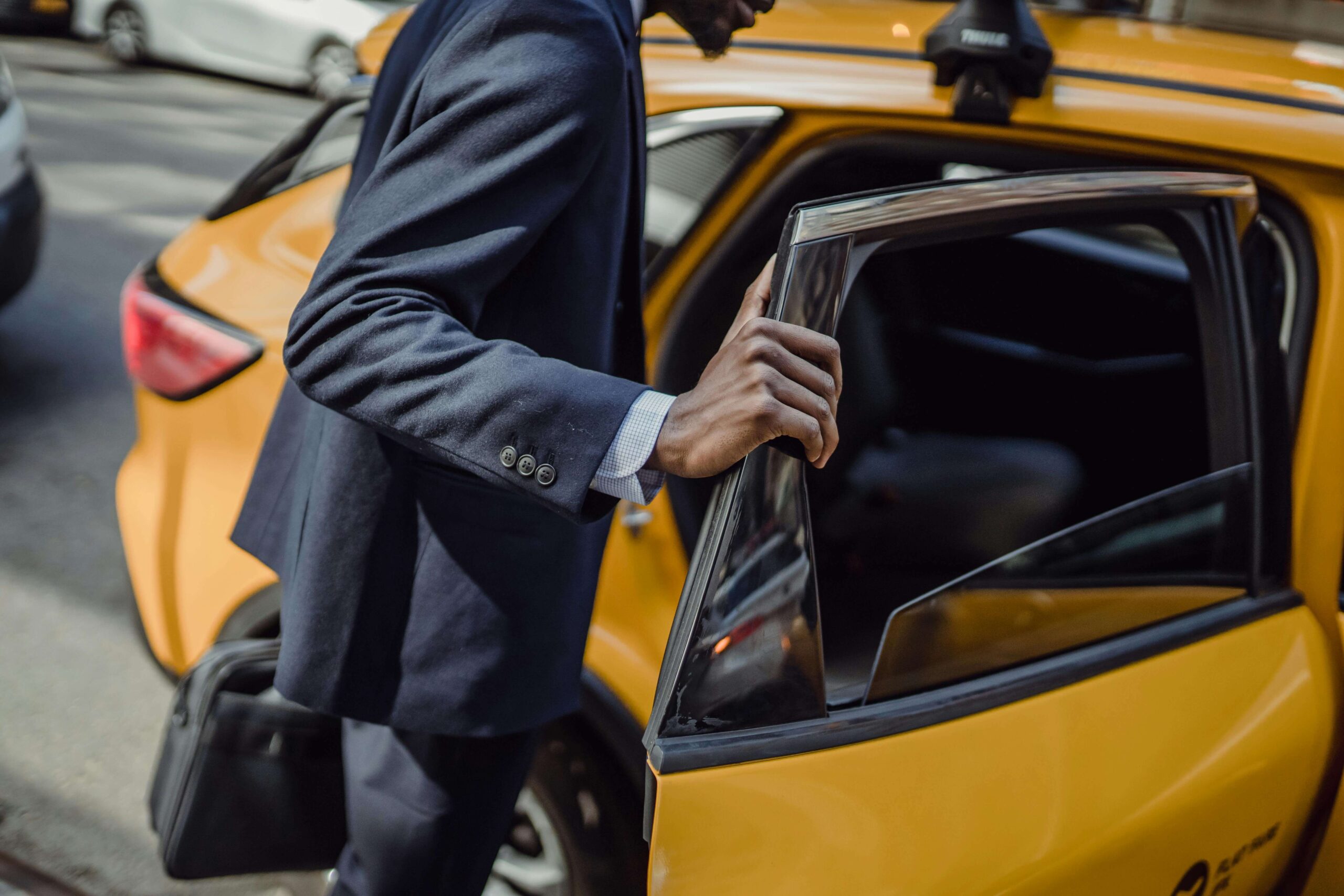 A man in a suit opening the door of a yellow car