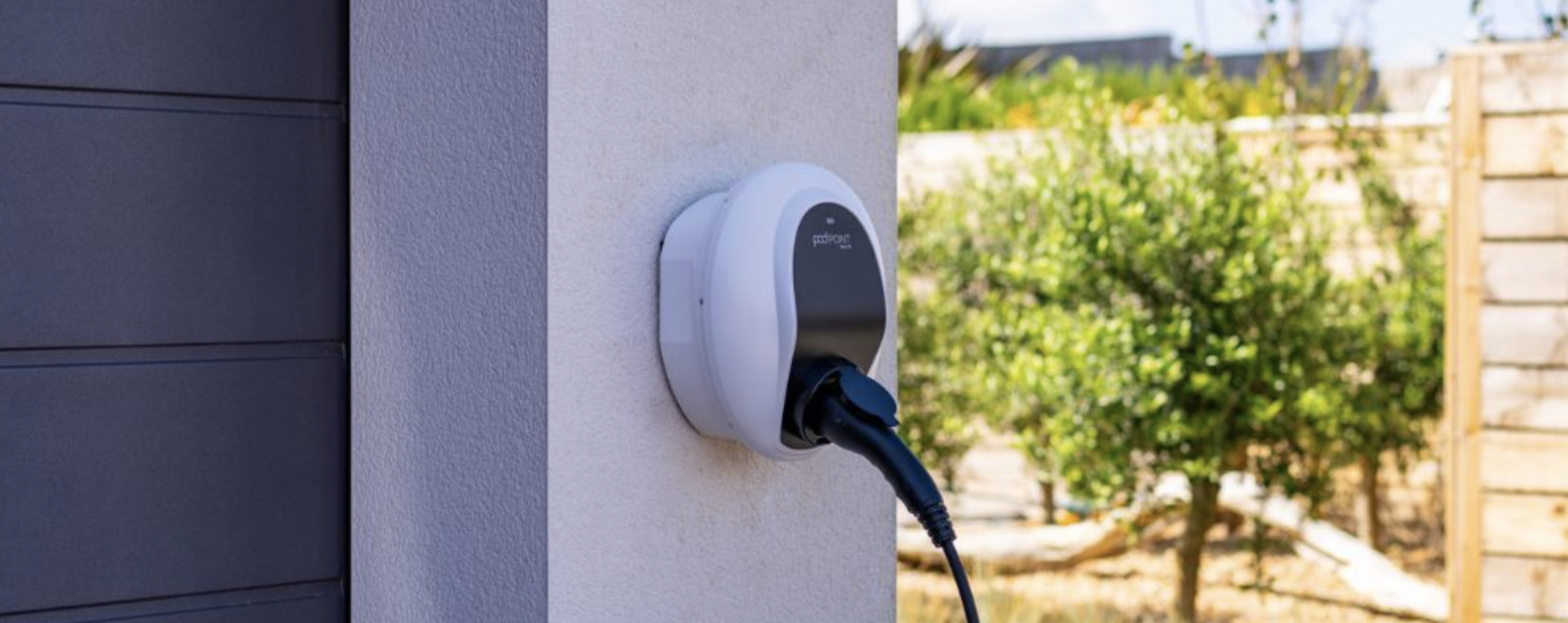 A white and black Pod Point wall charger mounted on a cream wall