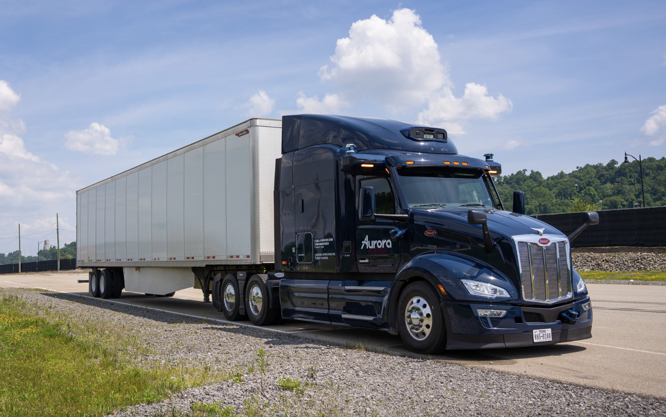 A truck with the Aurora logo on the cab door, the cab is dark blue and the lorry is white