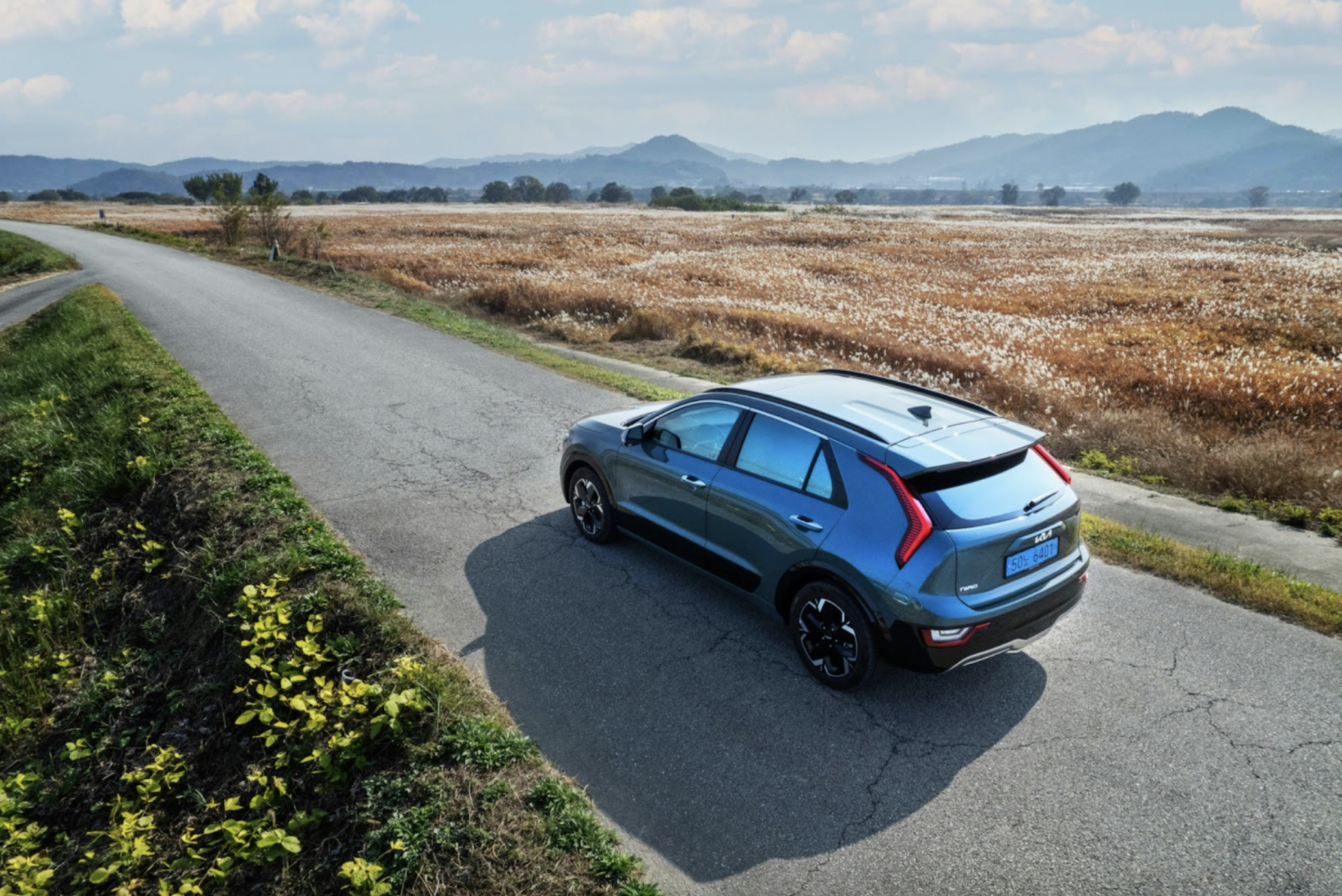 A blue car driving away from the camera, on a road through countryside fields