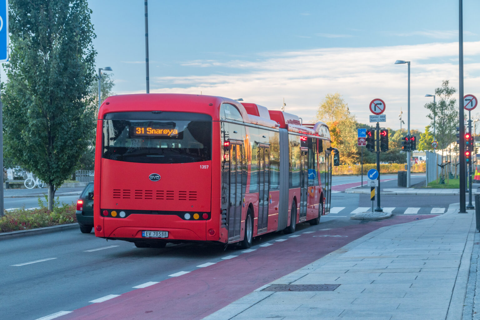 Red articulated public transport bus in Oslo, Norway, on route 31 to Snarøya, driving on a dedicated bus lane with traffic signals in the background.