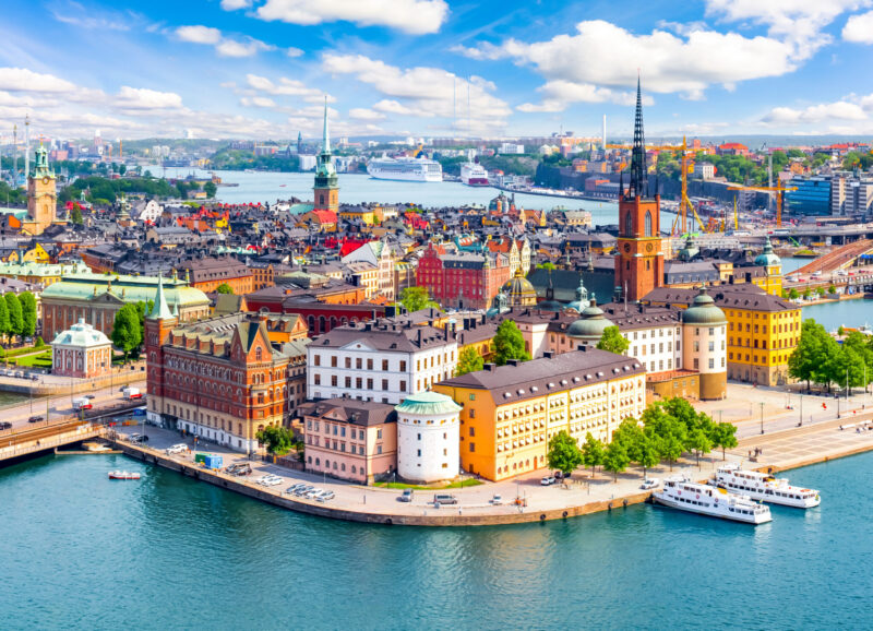 Scenic aerial view of Stockholm, Sweden, featuring colorful historic buildings, waterfront, and landmarks under a bright blue sky.