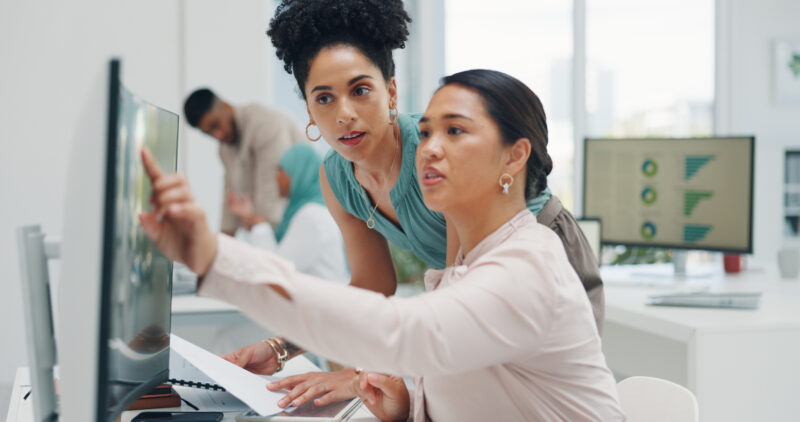 Two women in an office pointing at a computer screen while reviewing fleet safety data