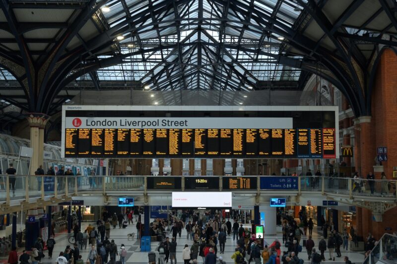 Crowded concourse at London Liverpool Street station beneath a large departures board and a glass and iron roof